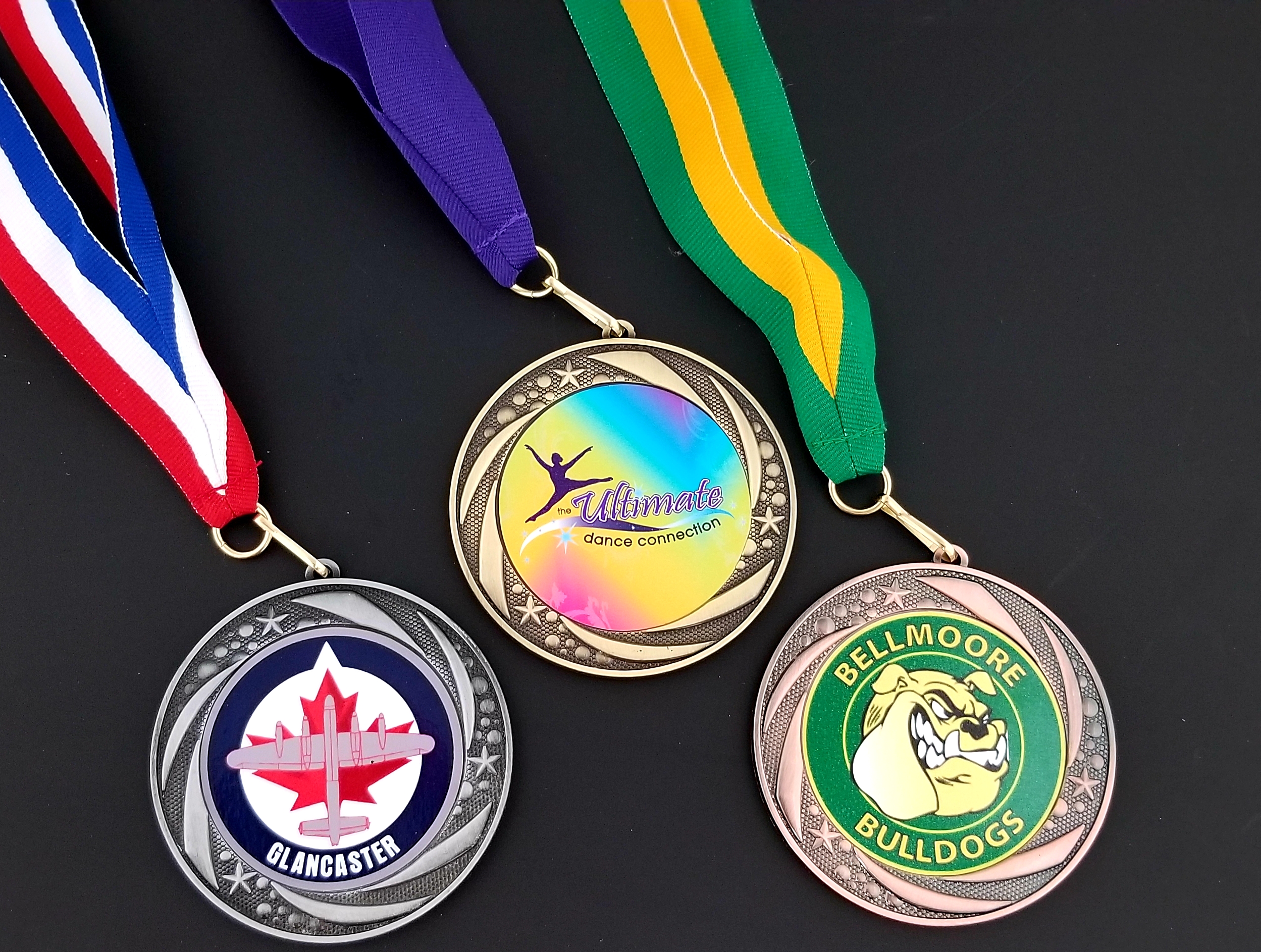 A collection of custom-designed sports medals for Glancaster hockey, Bellmoore Bulldogs, and Ultimate Dance Connection.
