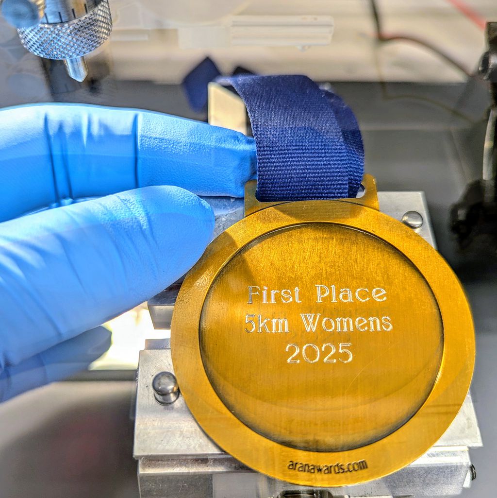 An engraver's hands carefully placing a custom sports medallion into a Gravotech engraving machine at Aran Awards.